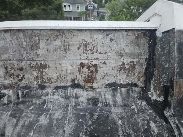 Parapet wall at 2105 Mt Vernon Ave after power washing, exposing the deteriorated wall surface and previous asphalt flashing repairs