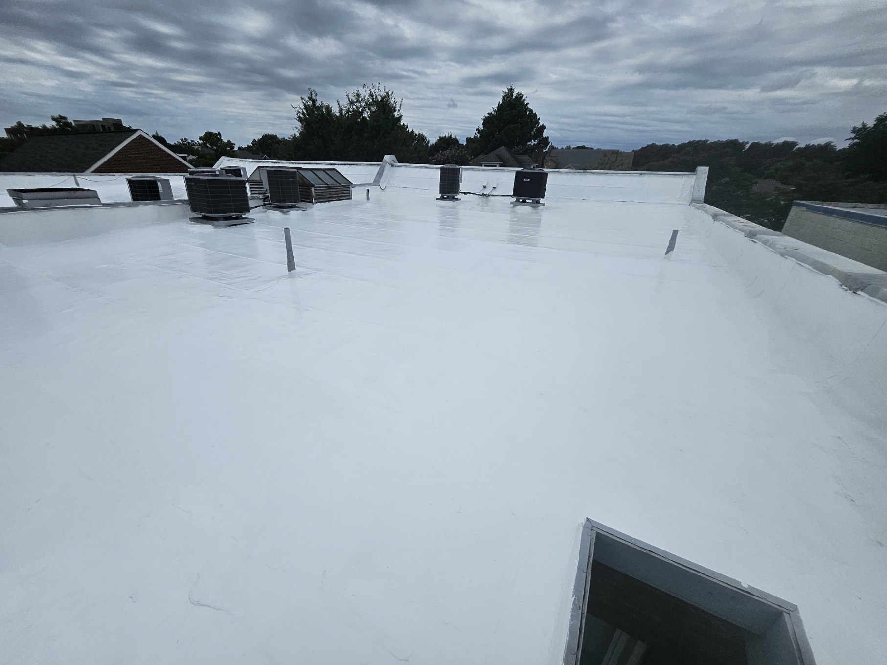 Seamless white silicone roof surface at 2105 Mt Vernon Ave under overcast sky, showing the coated field, curbs, and parapet terminations