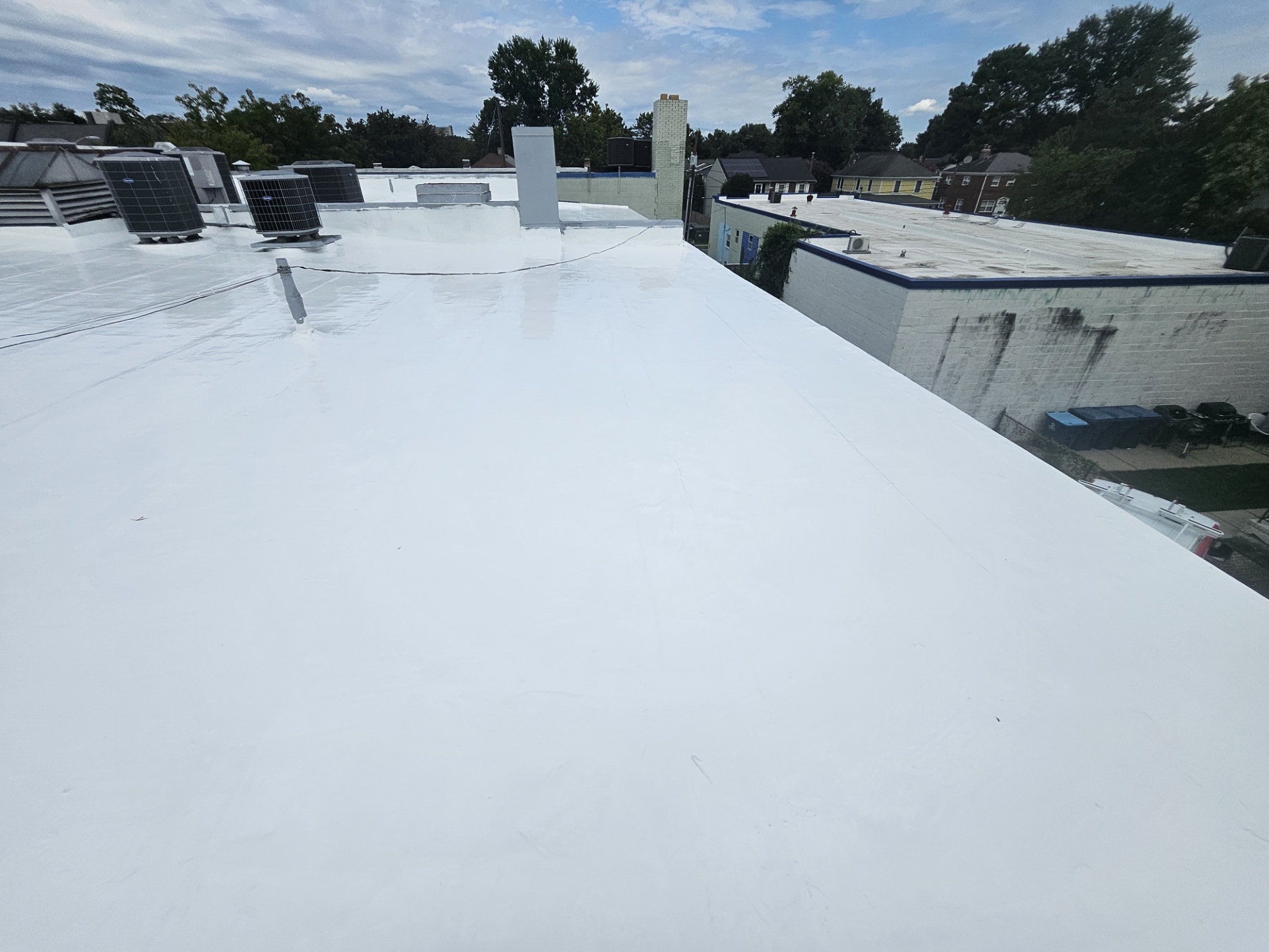 Finished reflective white silicone roof restoration at 2105 Mt Vernon Ave, contrasted against the untreated adjacent building roof