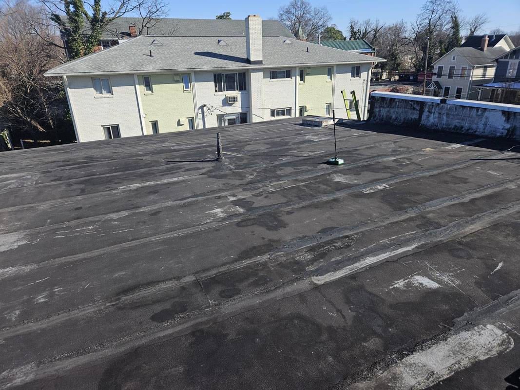 Wide view of the aged modified bitumen roof field at 2105 Mt Vernon Ave showing lap seams, previous repairs, and dark ponding stains before restoration