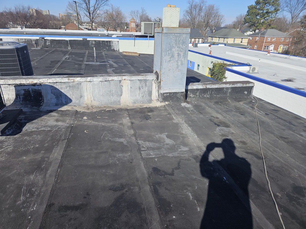 Aged modified bitumen roof at 2105 Mt Vernon Ave with rooftop HVAC unit, masonry flue, and weathered parapet walls before silicone restoration