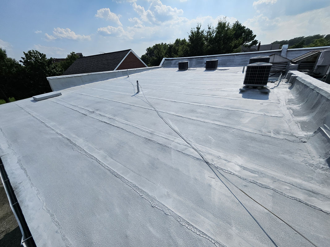 PM P-160 asphalt bleed-block primer applied across the modified bitumen roof field at 2105 Mt Vernon Ave, leaving a uniform light grey surface