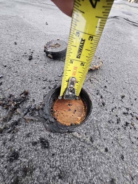 Full-depth roof core cut at 2330 Columbia Pike with a tape measure recording the assembly thickness and the wood deck visible at the base of the core