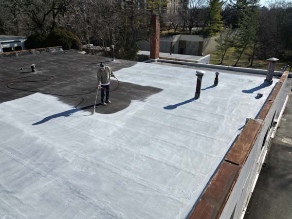 GoTech Roofing technician spray applying PM P-160 asphalt bleed-block primer across the modified bitumen roof at 2330 Columbia Pike