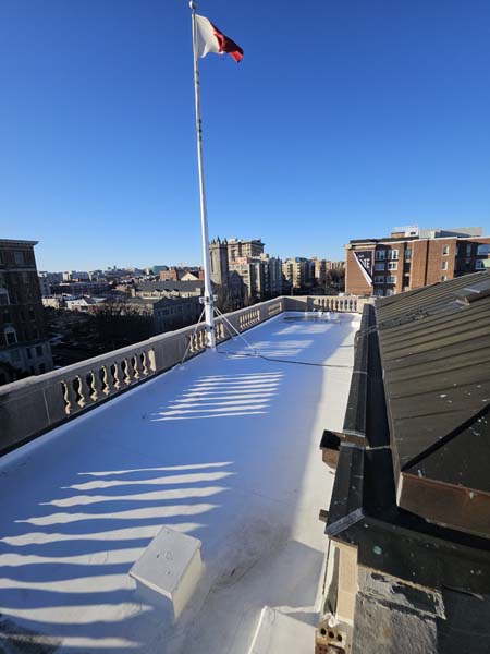 Completed TPO roof behind the stone balustrade at 1530 P St NW, with the embassy flagpole above the finished white membrane