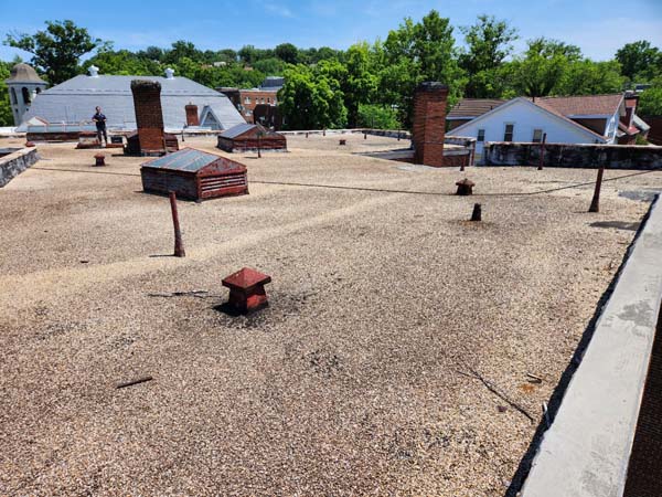 Ballasted roof at 2801 Pennsylvania Ave SE showing brick chimneys, vent penetrations and a metal equipment housing before tear-off