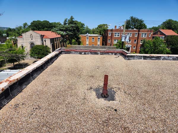 Stone-ballasted modified bitumen roof at 2801 Pennsylvania Ave SE before replacement, with a corroded vent stack and rusted parapet coping