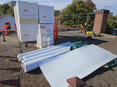 Polyisocyanurate insulation bundles and rolls of white TPO membrane staged on the ballasted roof at 2801 Pennsylvania Ave SE